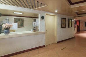 Zona de recepció amb taulell de recepció, un rellotge, quadres a la paret i un paviment de rajoles.