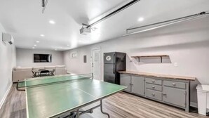 A modern kitchen with a green ping pong table, grey cabinets, and a built-in oven.