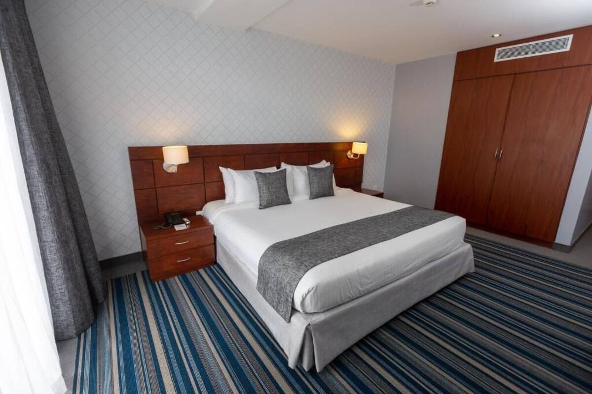Habitación de hotel con una cama grande, dos mesitas de noche, un armario y una alfombra estampada.