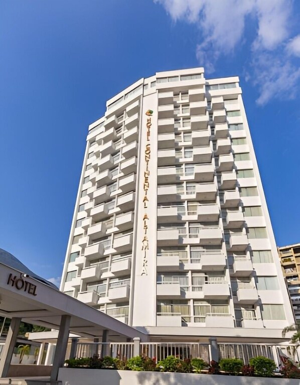 Un hotel moderno de gran altura con varios balcones, cielo despejado y un cartel que indica que es un hotel.