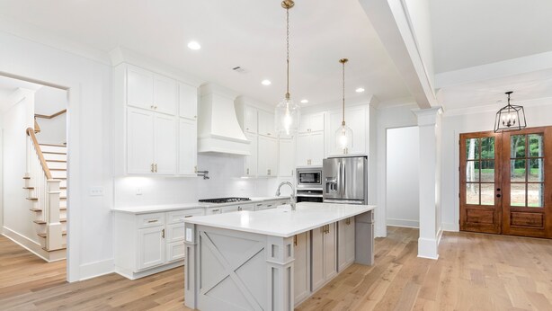 Una cocina amplia con armarios blancos, una isla grande, electrodomésticos de acero inoxidable y una escalera de madera.