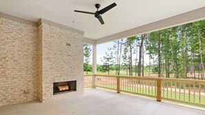 Una habitación amplia con pared de ladrillo, chimenea y balcón con vistas a árboles.