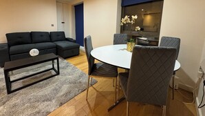 Una sala de estar moderna con un sofá seccional negro, una mesa de comedor redonda con cuatro sillas y una mesita auxiliar.