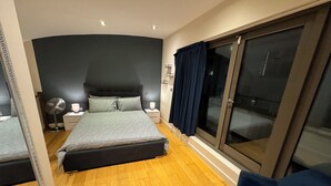 Un dormitorio con cama, mesita de noche, lámpara y un amplio ventanal corredera a un balcón.