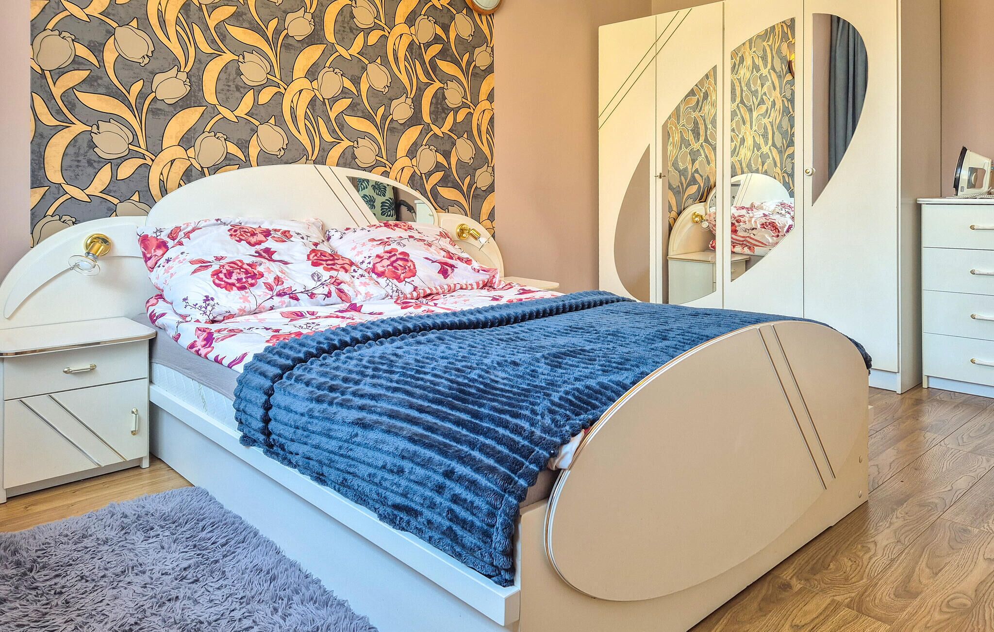 Une chambre à coucher comprenant un lit, des tables de chevet, une commode, un miroir et un papier peint à motifs.