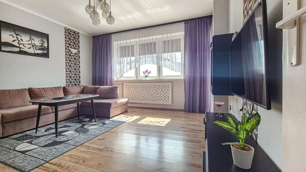 A living room with a sofa, coffee table, and a TV mounted on the wall. - 2 bedroom cozy home in Szczecin (Szczecin)