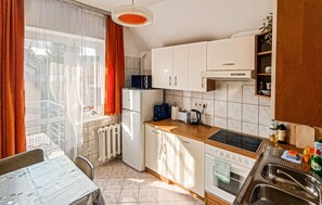 Uma cozinha compacta com armários brancos, bancada, pia e janela com cortinas.