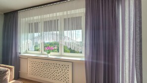 A room with a large window, white curtains, and a radiator. - 2 bedroom cozy home in Szczecin (Szczecin)