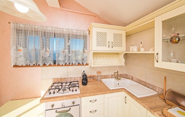 A kitchen with a gas stove, a sink, and a window with decorative curtains.