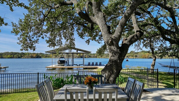An outdoor dining area with a table and chairs, a gazebo, and a view of a lake. - Packsaddle Point Luxury Lakefront w/Pool+Guest House (Kingsland)