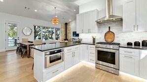 A modern kitchen with white cabinetry, stainless steel appliances, and a large island. - Packsaddle Point Luxury Lakefront w/Pool+Guest House (Kingsland)