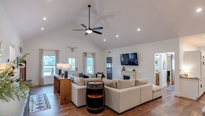 Ein geräumiges Wohnzimmer mit hoher Decke, Kamin, großem Fernseher und Couchtisch aus Holz.