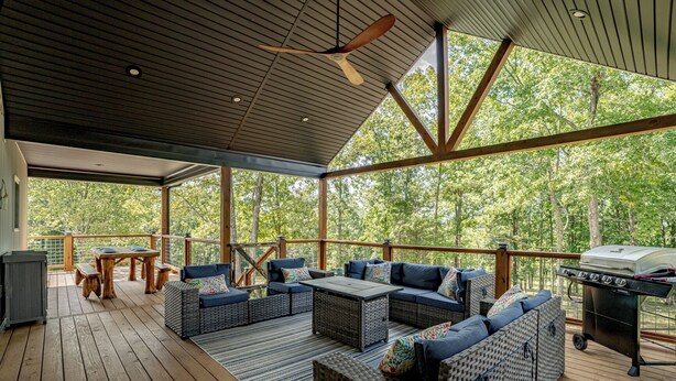 Eine überdachte Terrasse im Freien mit Holzboden, einem Grill und Sitzbereichen mit Kissen.