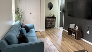 A living room with a blue sofa, a television, a dark wall, and a wooden floor.