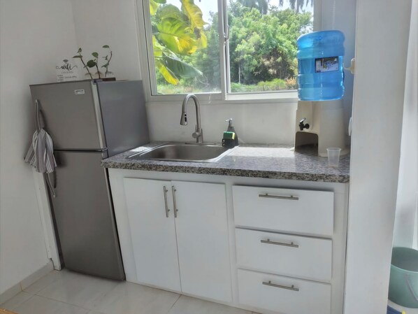 Una cocina con un refrigerador de acero inoxidable, un fregadero y una ventana con vista a la vegetación.