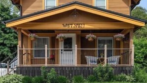 Een houten huis met twee verdiepingen, een veranda, een klein voorraam en een brievenbus.