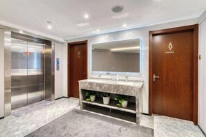 Un baño moderno con tocador de mármol, un espejo grande, una puerta de madera con la etiqueta 'WOMEN'S' y un ascensor.