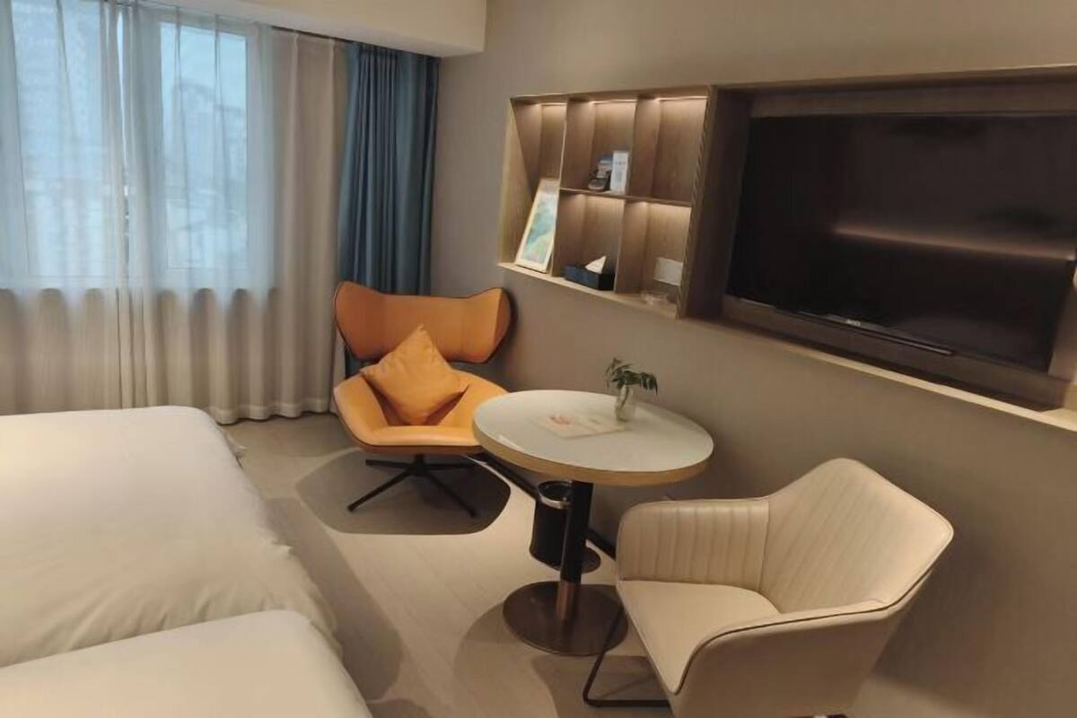 Une chambre d’hôtel avec un lit, une table ronde, un canapé, une télévision et une étagère avec divers objets.