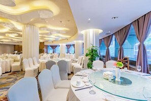 A hotel dining area with round tables, white chairs, and a glass-top table. - Hangzhou West Lake Enjoyor Hotel (Hangzhou)