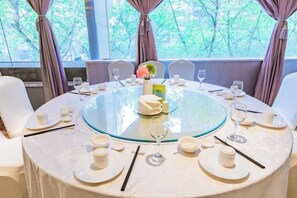 Una mesa de comedor redonda con cubierta de vidrio, rodeada de sillas blancas, dispuesta con platos, tazas y palillos.