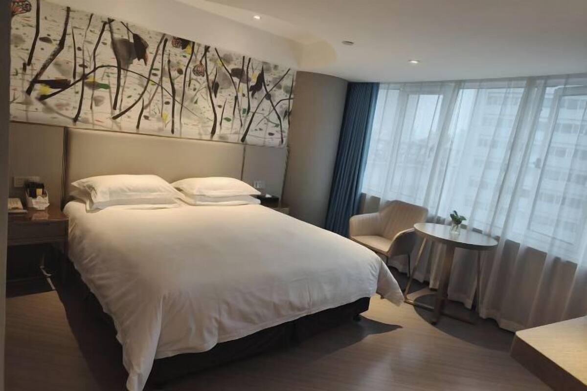 Une chambre d’hôtel avec un grand lit, une petite table ronde, une chaise et un tableau accroché au mur.