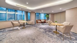 Une chambre d’hôtel moderne avec un sol en marbre, de grandes fenêtres et un coin salon doté de tables et de chaises rondes.