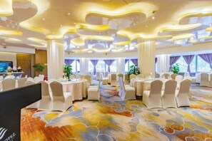Un salón de banquetes con mesas redondas, sillas blancas y una alfombra estampada.