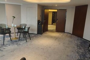 Ein Hotelzimmer mit Teppichboden, einem Essbereich mit Stühlen und Tisch sowie einer Tür zu einem weiteren Raum.