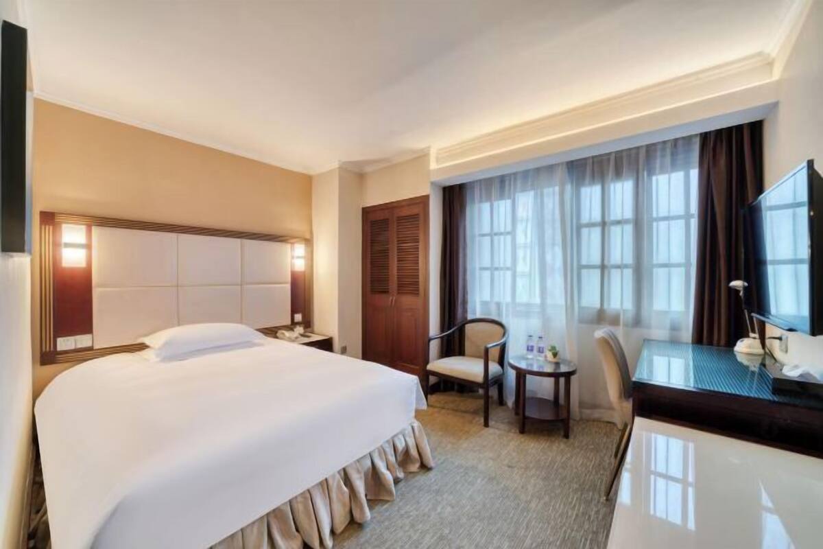 Une chambre d’hôtel avec un grand lit, un bureau avec une chaise, une télévision et une fenêtre avec des rideaux.