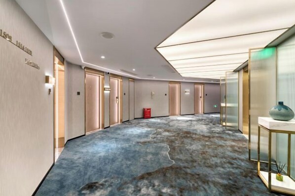 A hotel corridor with a unique blue carpet, doors, and a vase on a table.