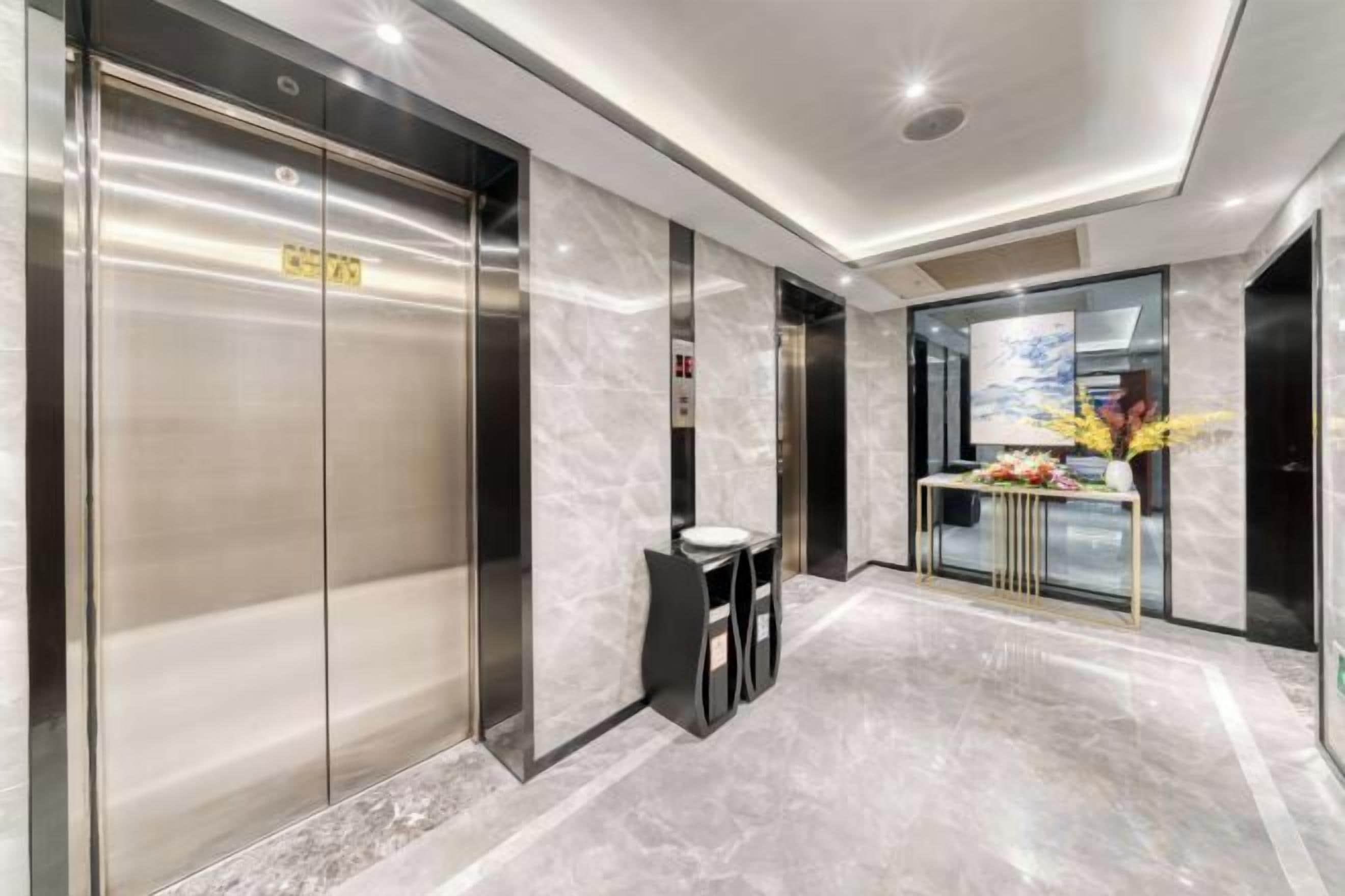 A modern elevator with a digital display, a marble floor, and a reception desk with a vase of flowers.
