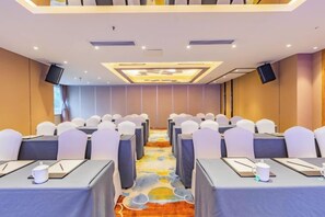 Un salón de conferencias con filas de mesas, sillas y suelo alfombrado.