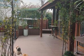 Una terraza de madera con una pérgola, plantas en macetas y un espacio de estar.