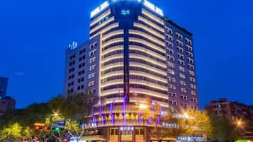 A multi-story hotel with a curved facade, illuminated signage, and a ground-level entrance with a covered walkway.