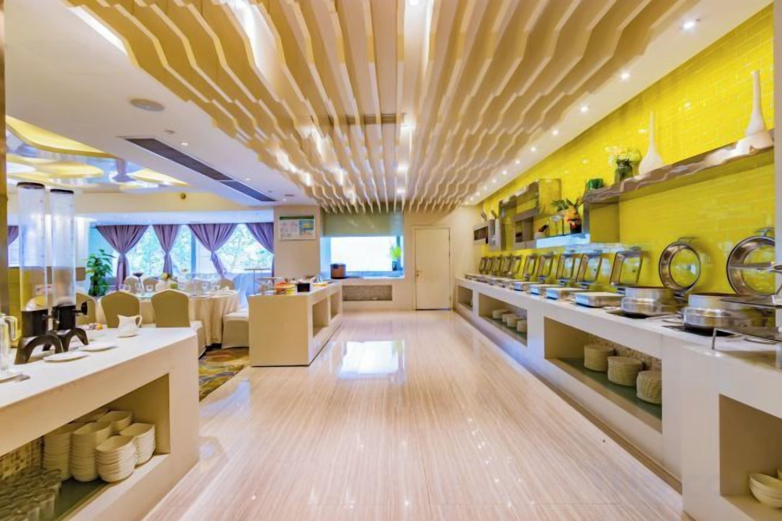 Un lobby moderno de hotel con una recepción central, un área de buffet con exhibición de alimentos y una zona de estar con mesas y sillas.