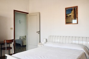 A bedroom with a bed, a chair, a nightstand, a wall-mounted lamp, and a door leading to another room.