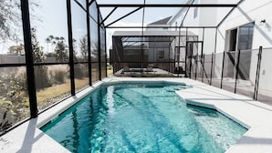 Ein moderner Außenpool mit Glasveranda, eine Terrasse mit Sitzgelegenheiten und Blick auf ein Wohngebäude.