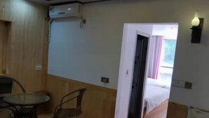 Una habitación con una cama, una mesita y una silla. Se ve una puerta que da a otra estancia.