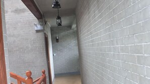 Un pasillo estrecho con paredes de ladrillo, piso de madera y barandilla de madera a la izquierda.
