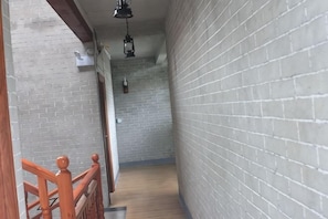 Un couloir étroit aux murs de briques, avec un plancher en bois et une rambarde en bois sur le côté gauche.