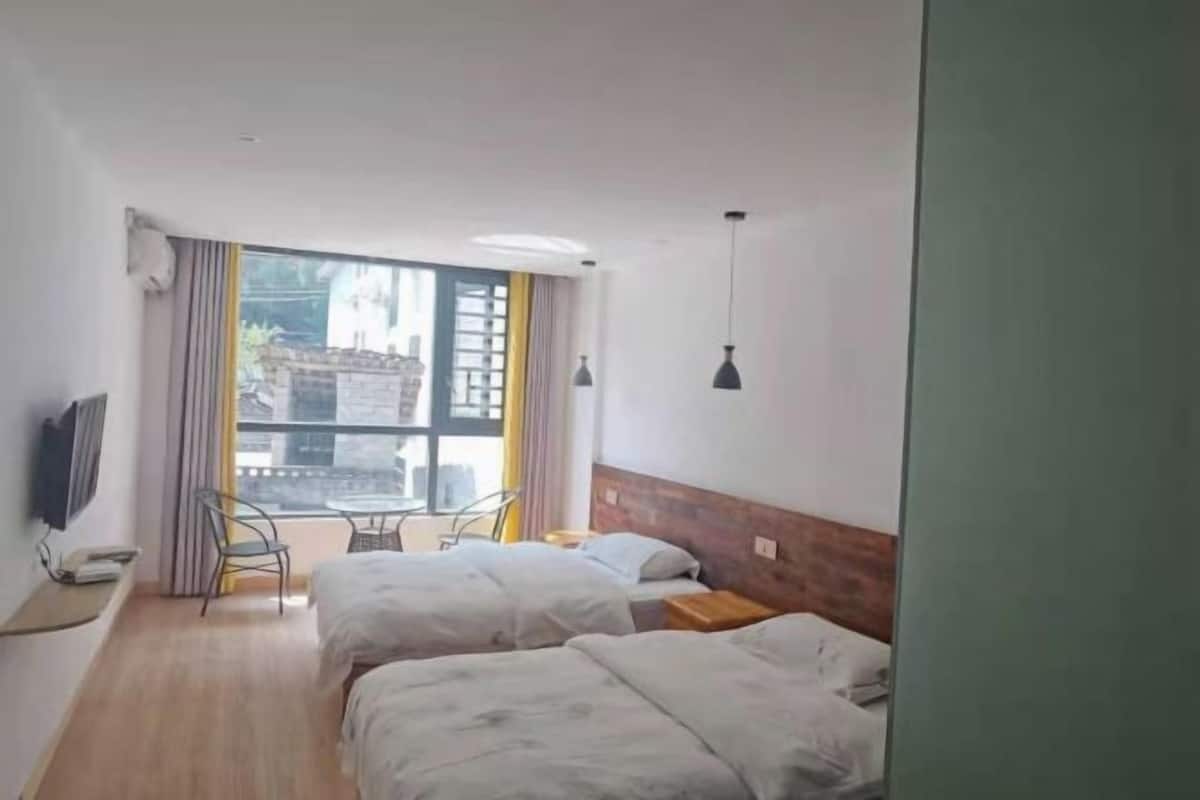 Une chambre d’hôtel avec deux lits, une télévision, une fenêtre avec des rideaux et une petite table avec des chaises.