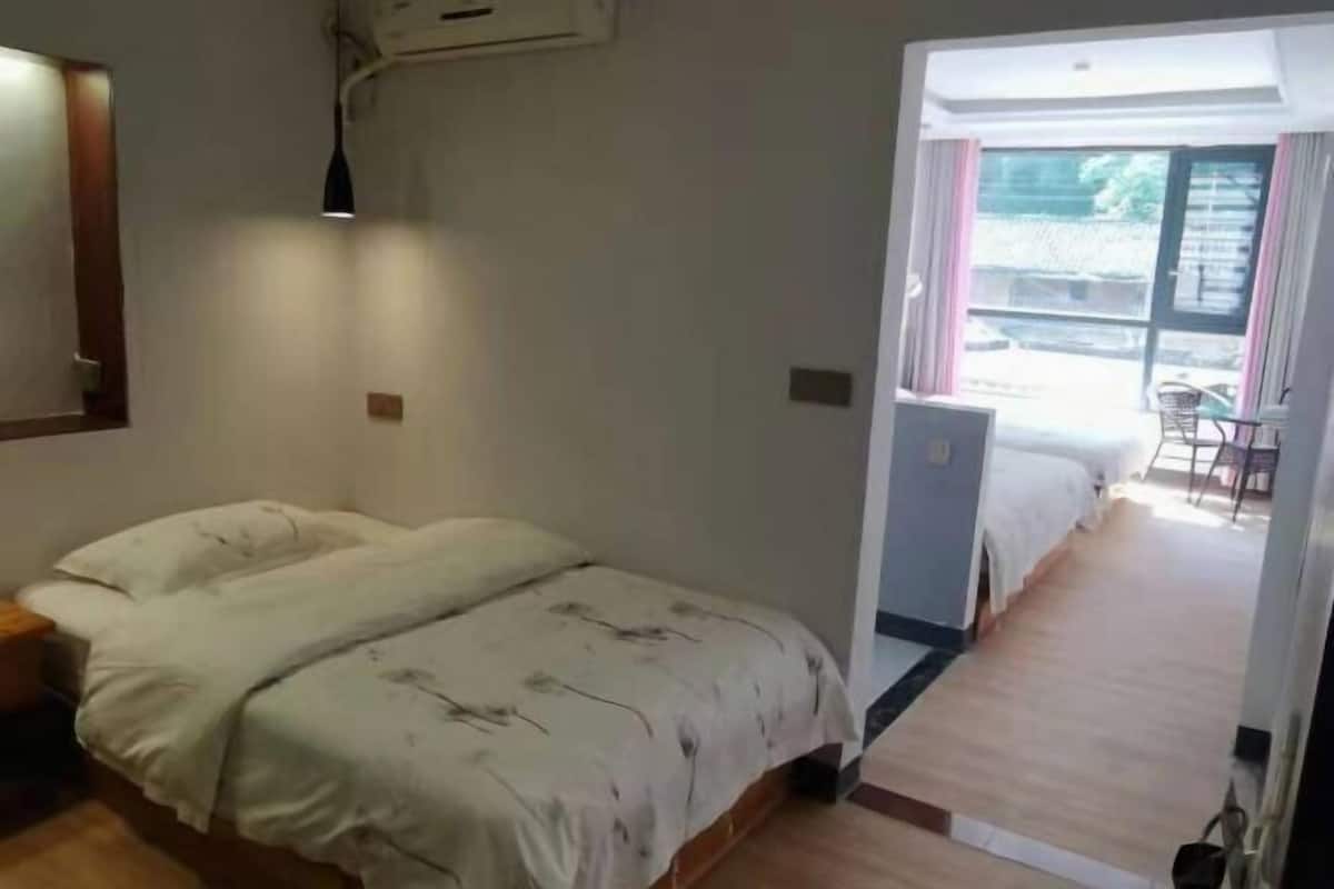 Une chambre à coucher avec un lit, un bureau et une chaise. Il y a une fenêtre avec des rideaux et une vue sur l’extérieur.