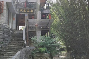 A traditional building with a stone staircase leading to a wooden entrance, surrounded by greenery. - Gujia Inn (Zhaoping)