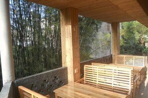 Une terrasse en bois avec une table et des bancs, entourée de murs en bambou et en pierre.