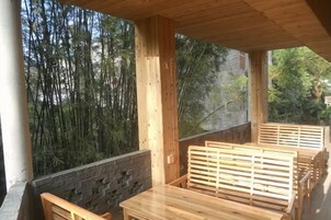 Una terraza de madera con una mesa y bancos, rodeada de bambú y muros de piedra.