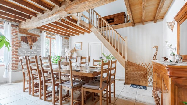 Un coin repas avec une table et des chaises en bois, un escalier et un mur en briques.