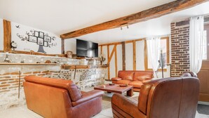Un salon rustique avec des poutres apparentes, une cheminée en briques, des canapés en cuir et un téléviseur à écran plat.