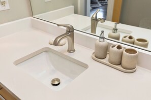 A bathroom with a white sink, a modern faucet, and a mirror reflecting the sink and a set of beige ceramic cups. - Spacious 2BR 2BA with Parking, Gorgeous Skyline View, and Direct Skywalk Access! (Des Moines)