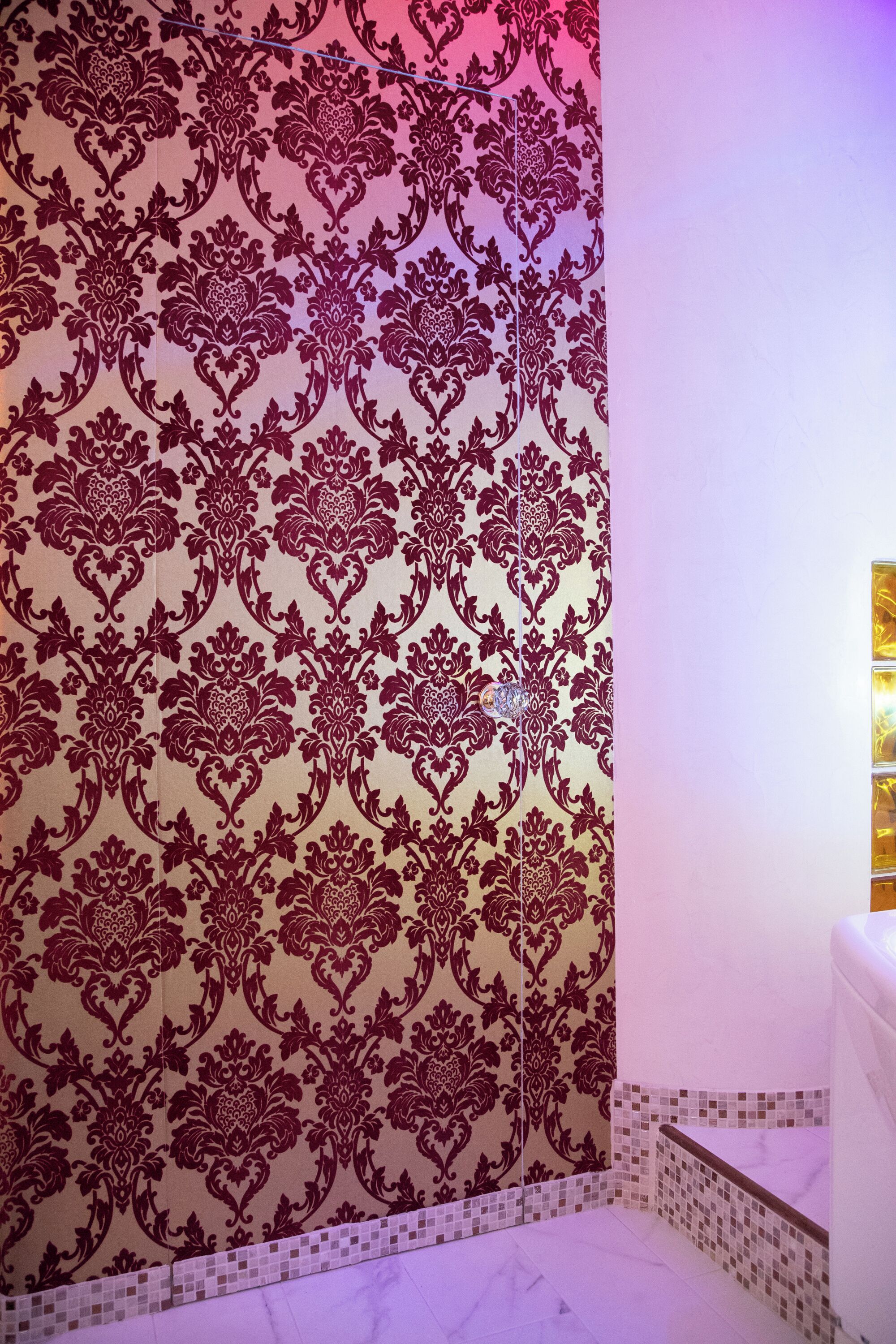 Un bagno con carta da parati decorata, pavimento piastrellato e vasca da bagno bianca.