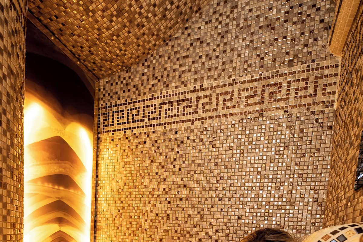 A person relaxing in a tiled bathtub with a mosaic design.